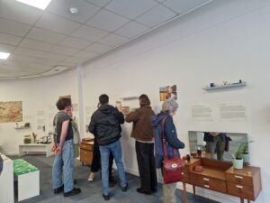 A group of adults standing in a circle in a room looking at exhibition posters and displays.