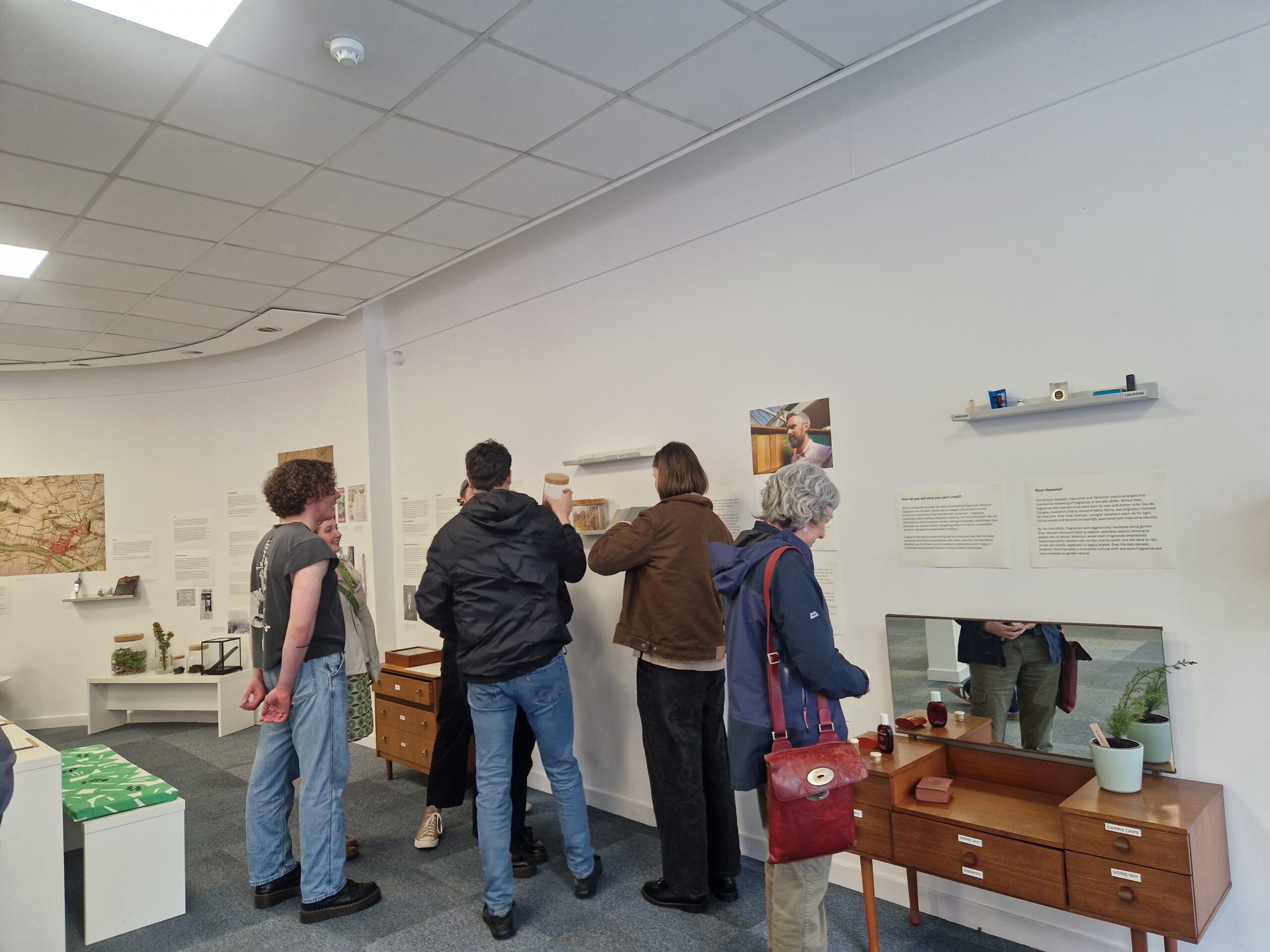 A group of adults standing in a circle in a room looking at exhibition posters and displays.