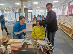 A woman in a yellow jumper and two adults beside her with some schientific equipment in the foreground.