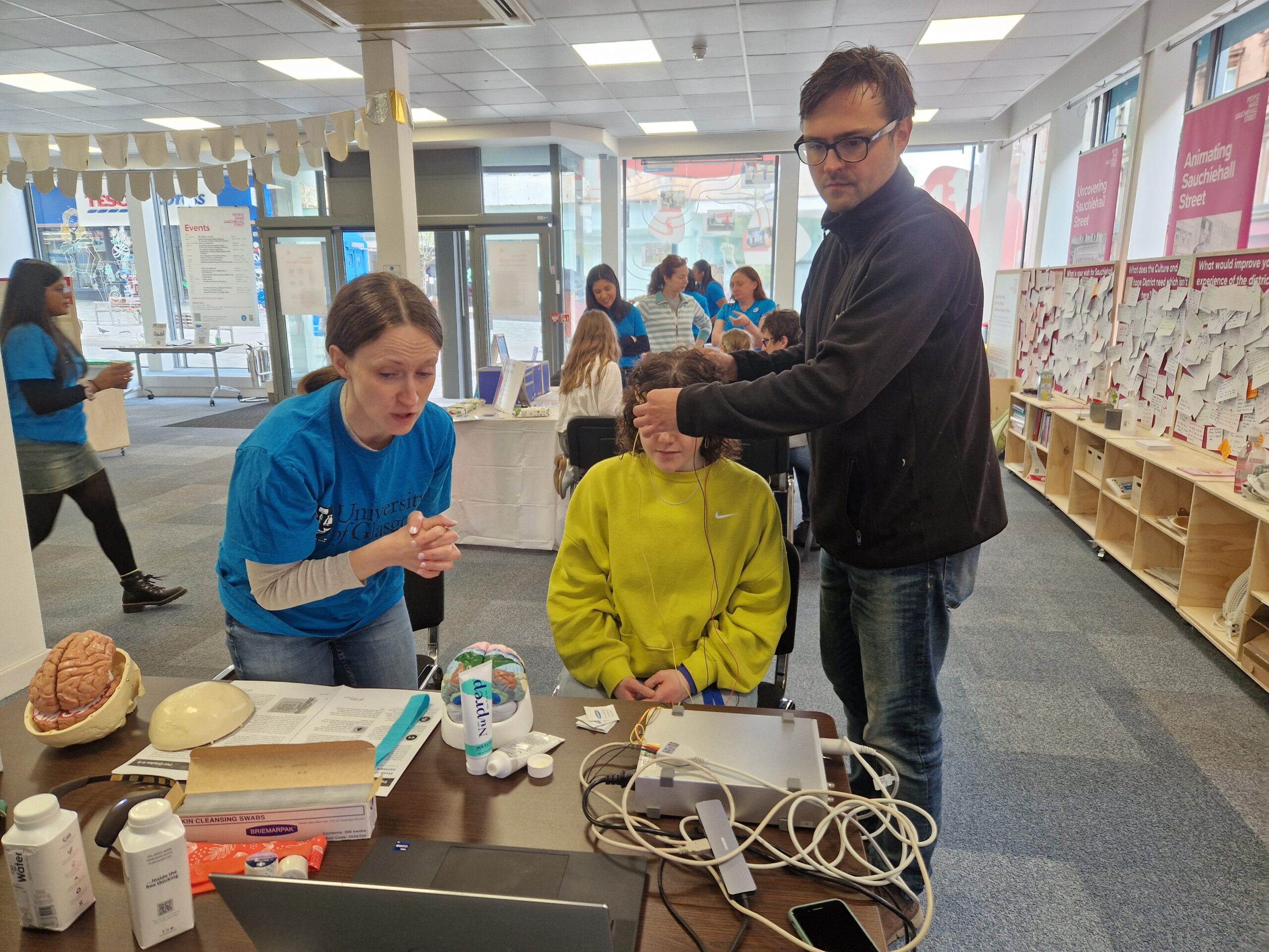 A woman in a yellow jumper and two adults beside her with some schientific equipment in the foreground.