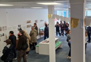 People in a large room looking at exhibition materials and chatting to each other.