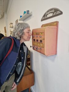 A woman in a blue jacket leaning forward and sniffing a pink, metal 'perfumatic' scent dispenser.