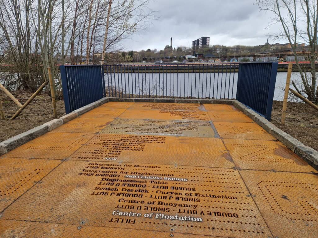 A large slab of ironwork, engraved with writing. A river can be seen in the background.
