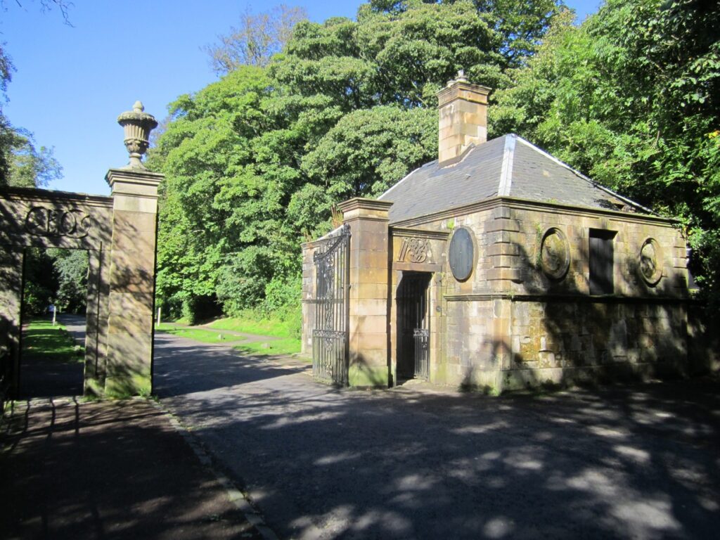A small, stone built house, with gate piers in the foreground on a sunny day with trees in the background.