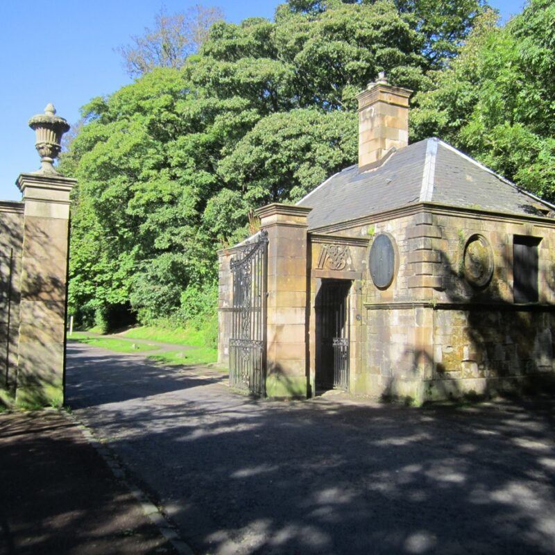 A small, stone built house, with gate piers in the foreground on a sunny day with trees in the background.