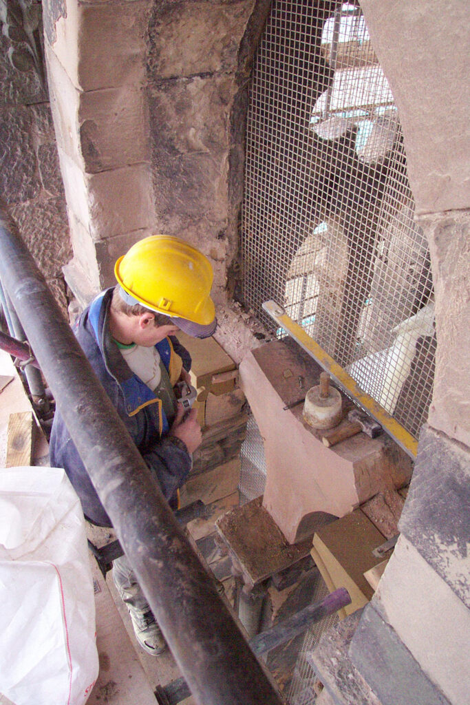 A man in a yellow hard hat repairing damaged stonework.
