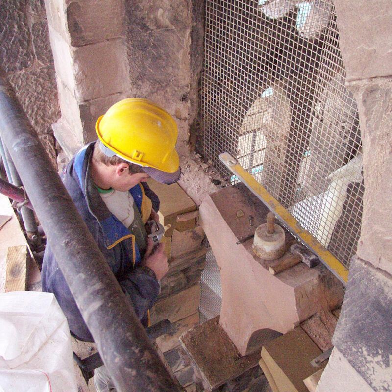 A man in a yellow hard hat repairing damaged stonework.